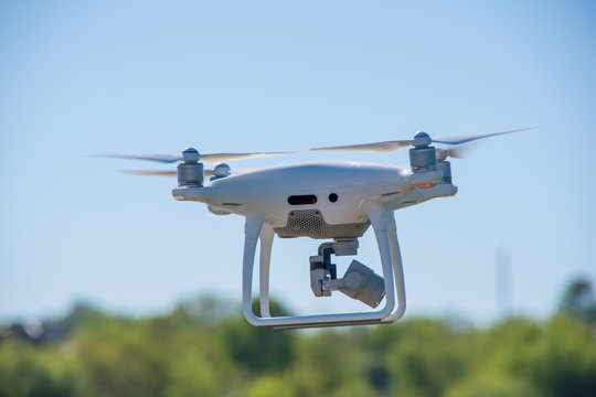 The modern drone, quadrocopter is in the air against the background of the sky and grass