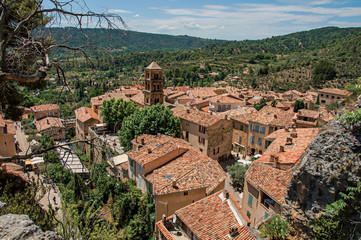 Fototapeta na wymiar View of trees, house roofs and belfry under sunny blue sky in the charming village of Moustiers-Sainte-Marie. Located in the Alpes-de-Haute-Provence department, Provence region, southeastern France