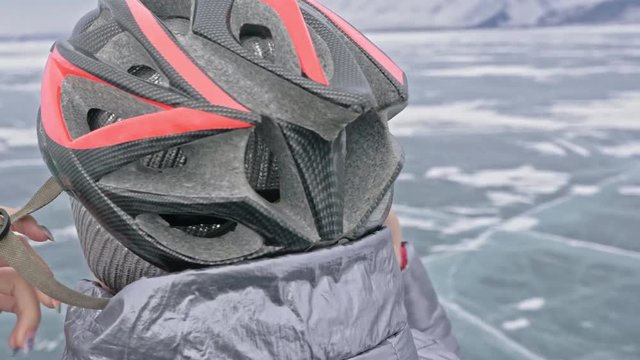 Woman is wearing sports equipment. The girl is dressed in a silvery down jacket, cycling backpack and helmet. Ice of the frozen Lake Baikal. The tires on the bicycle are covered with special spikes