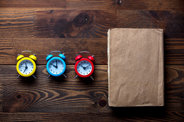 Three colorful alarm clocks and book on wooden table