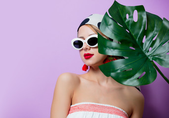 Fototapeta premium Portrait of beautiful style woman in sunglasses with palm leaf on purple background