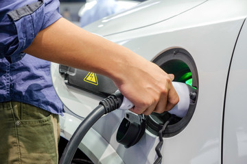 Close-up asia men hands who are fueling a new vehicle electrification via rechargeable electricity machine, Electric cars are a new innovation in the future, built to replace cars powered by oil.
