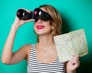 Young girl with binoculars and map looking for something on green background