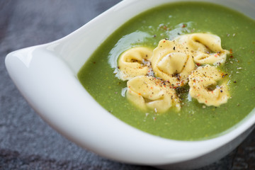 Closeup of broccoli cream-soup with tortellini served in a white bowl, selective focus