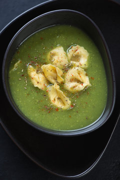 Closeup of cream-soup with broccoli topped with tortellini, view from above, vertical shot