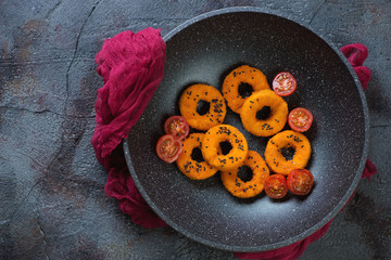 Wok pan with roasted breaded calamari rings, top view on a weathered asphalt background, horizontal shot with space
