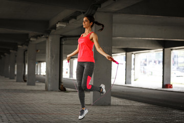 Female in sports outfit workout on the street with jump rope. - obrazy, fototapety, plakaty