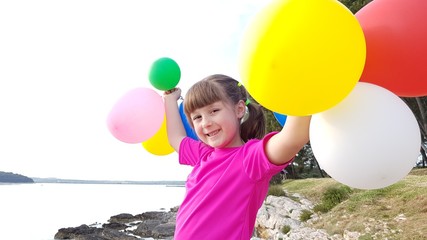 Bambina che gioca con i palloncini colorati al tramonto