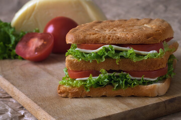 Home sandwich on wooden board, tomatoes, lettuce and cheese.