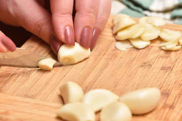 Obraz na płótnie Canvas Female hands with a knife chop fresh garlic on a cutting board. Close-up