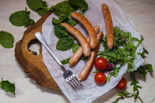 Grilled sausages with cherry tomatoes ,spinach and arugula on a wooden background in rustic style