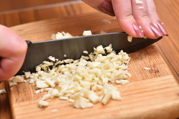 Female hands with a knife chop fresh garlic on a cutting board. Close-up