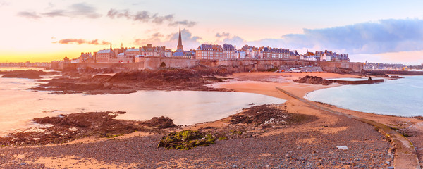 View from the tidal island of Grand Be to the city of Saint Malo and causeway shortly before the tide at sunrise. Saint-Maol is famous city of Privateers is known as city corsaire, Brittany, France. - obrazy, fototapety, plakaty