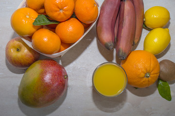 Fresh healthy tropical fruits. Summer food, vitamins concept.Basket of ripe mandarins,apple,mango,red bananas,lemons,orange and kiwi with glass of juicy.