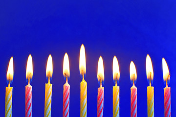 Ten yellow and pink burning birthday candles on bright blue background.