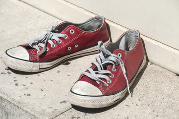Abandoned heavy used old grunge weathered red sport sneakers on street stone surface