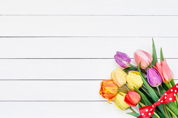 Colorful tulips bouquet decorated with ribbon on white wooden background. Copy space, top view. Mothers Day, Birthday, Valentines Day concept.