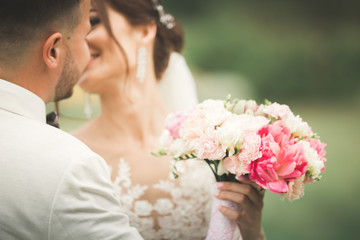 Stylish couple of happy newlyweds walking in the park on their wedding day with bouquet