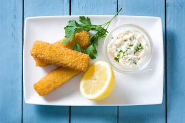 crispy fried fish fingers with lemon and sauce on blue wooden background. Top view