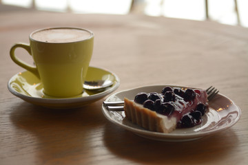 Cup of cappuccino coffee and blueberry cheese pie on table in cafe