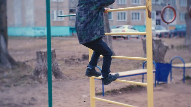 Boy crawling on the monkey bars in the yard of a city house. Games and walks on the Playground.