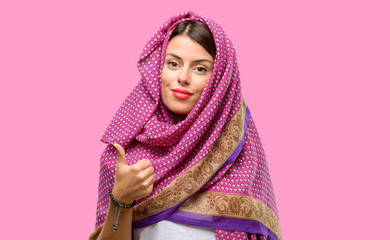 Young arab woman wearing hijab smiling broadly showing thumbs up gesture to camera, expression of like and approval