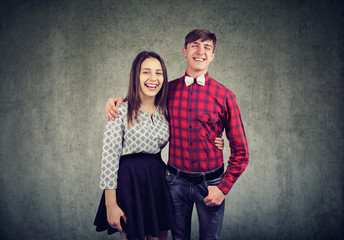 Cheerful young woman and man embracing one another, looking and smiling at camera