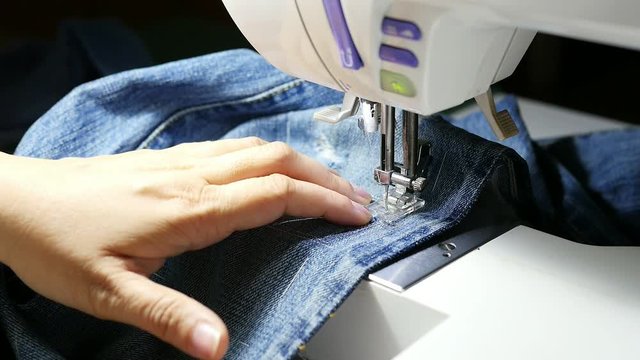 Woman doing jeans patchwork using sewing machine - home DIY sewing 