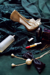 Women set - perfume, red lipstick, transparent bottle, jewelry with a bow and gold shoes on a green background