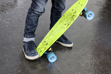 Legs of a child in black sneakers on a green skateboard