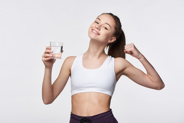 Sporty teen girl with glass of water in hand showing power gesture