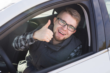 Young man test drive new car and showing thumbs up.