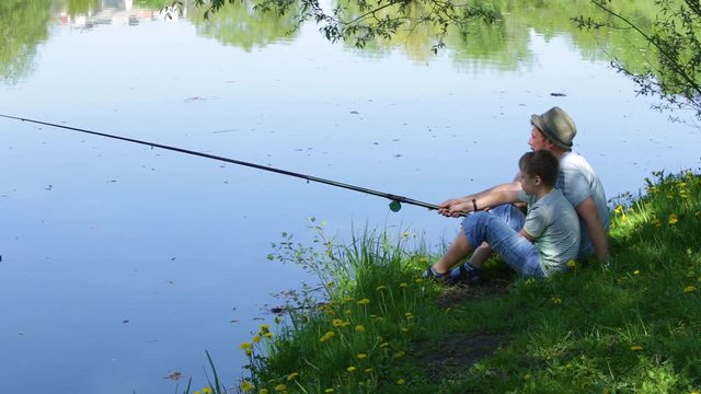 Happy family on summmer vacations concept. Father and son fishing together at river bank. Real time full hd video footage.