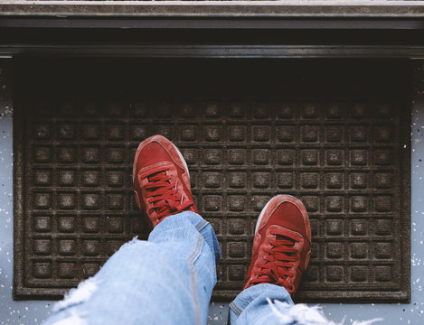 Red Sneaker Shoes Standing On Door Mat.  View Looking Down.