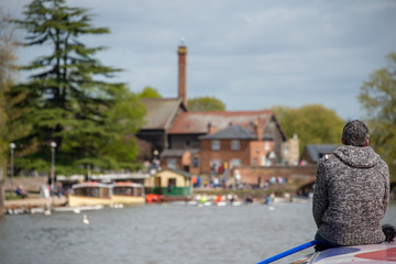 Retired lonely man sat on bow of boat wearing grey jumper with gray hair contemplating the beautiful willow trees on the river Avon in Great Britain and seeking solitude