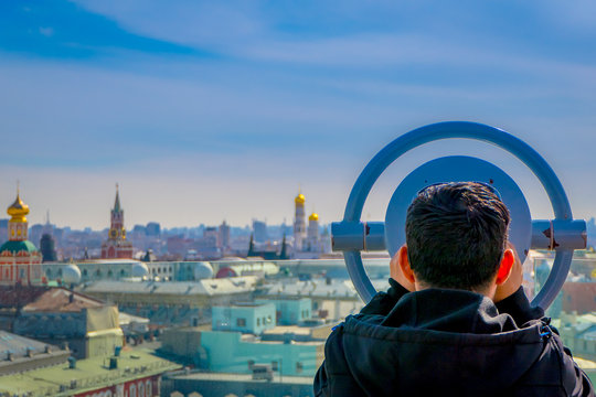 Close up of unidentified man using a metallic structure of coin operated binocular enjoying the city behind of Moscow business centers and skyscrapers and the international center of the city