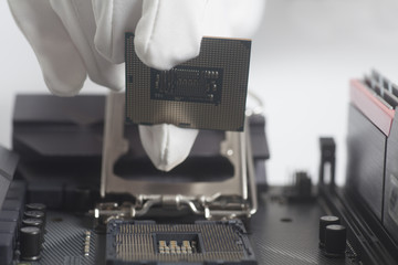 Computer technician wearing white gloves installing CPU into motherboard.