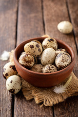 Fresh quail eggs in ceramic bowl on rustic wooden background