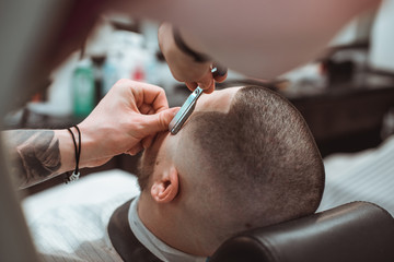 Making stylish curly haircut at salon closeup. Man sitting with closed eyes while barber shaving him with razor. Beauty, modern style, lifestyle, trend concept