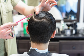 hairdresser does hair with red comb of handsome satisfied client in professional hairdressing salon