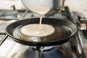 Cooking pancakes. The liquid dough from the ladle is poured onto a round pan