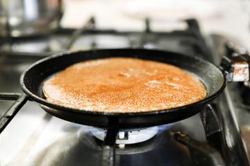 The process of making pancakes on a hot frying pan standing on a gas stove