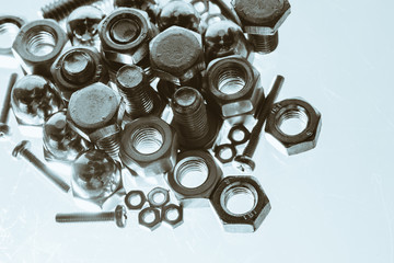 Art monochrome background from bolts and nuts close up in blue backlight. Macro photography of handful of fasteners. Copy space.