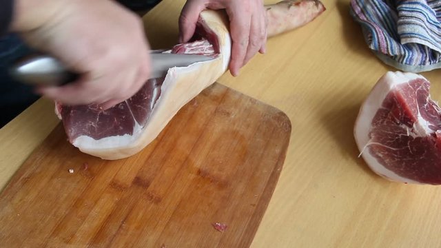 Man holding knife with hands, cutting, chopping, preparing pig raw, fresh meat steak for barbecue. Close up video footage of butcher cutting raw red bbq meat on cutting board.