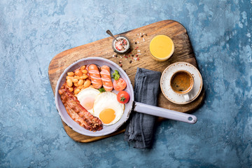 Traditional English Breakfast in the Frying Pan  Food on the Blue Background. Eggs, Sausages, Bacon, Beans,Toasts,Coffe and Orange juice