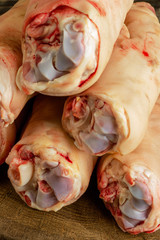 Raw and freesh pork feet or legs,over dark wooden board. They are stacked pile. Food meat shot. Vertical.