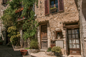 Fototapeta na wymiar Alley view with wooden doors and plants in Saint-Paul-de-Vence, a lovely well preserved medieval hamlet near Nice. Located in Alpes-Maritimes department, Provence region, southeastern France