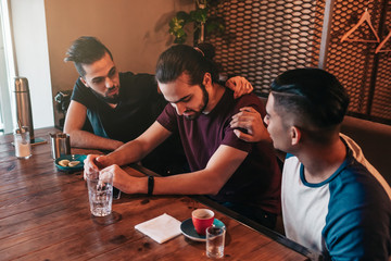 Supportive young men encourage their brokenhearted friend. Arabian guys cheer him up in restaurant....