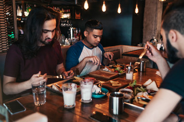 Multiracial friends eating breakfast in cafe. Young men chat while having tasty food and drinks. Guys hangout together