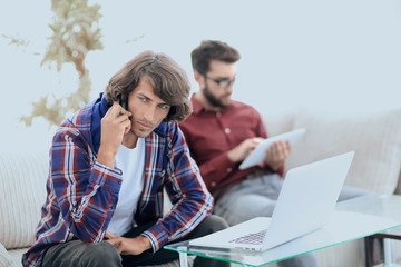 guy with a friend sitting on the couch, talking on the smartphone and searching for information on the Internet.